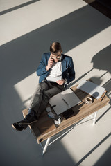 high angle view of fashionable businessman talking on smartphone while sitting at workplace