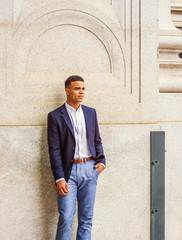 Portrait of African American Man in New York. Wearing blue blazer, white shirt, a male college student stands by vintage wall on street on campus, looks away, thinks. Filtered effect. .