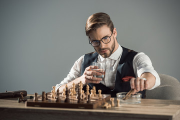 young businessman with glass of whisky and cigar playing chess