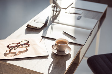 selective focus of eyeglasses on clipboard, cup of coffee and office supplies at workplace
