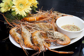 Grilled shrimp with sauce on white plate on the black floor.