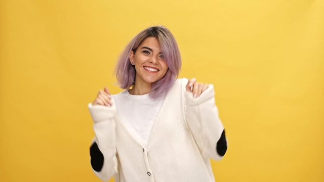 Cheerful woman in warm cardigan dancing and looking at the camera over yellow background