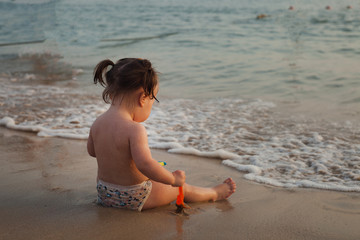 child playing on a sandy beach, sunset time, small waves