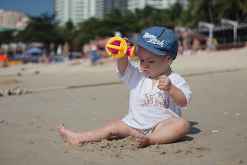 a child in sun-protective clothes and a headdress plays on a sandy beach on a clear hot day
