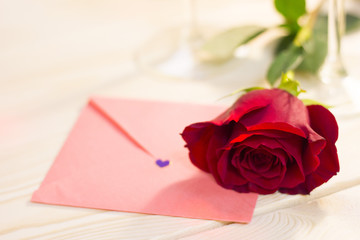 The concept of Love, Wedding, Proposal, Anniversary with a red velvet rose and a love letter on a light wooden table