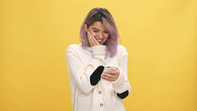Happy woman in warm cardigan writing message on smartphone over yellow background