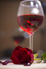 The concept of Love, Wedding, Proposal, Anniversary. A romantic evening with a glasss of red wine and a beautiful red velvet rose. Dark blurred background