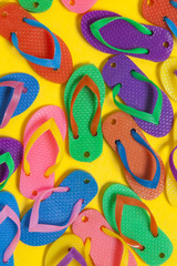 collection of colourful summer flip flop sandals on a bright yellow background