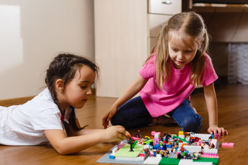 Two cute little children are playing with blocks happy girls at home funny lovely sisters