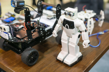 technology, entertainment, machining concept. close up of robotical devices that are placed on the wooden table, one is white and has legs and arms and even eyes