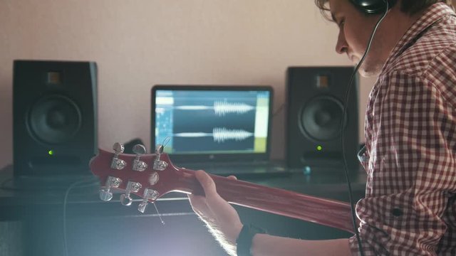 Young musician composes and records soundtrack playing the guitar using computer, headphones and keyboard