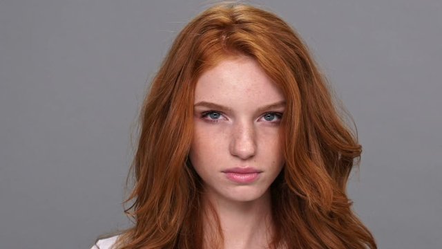 Close up view of smiling ginger woman in t-shirt looking at the camera over gray background