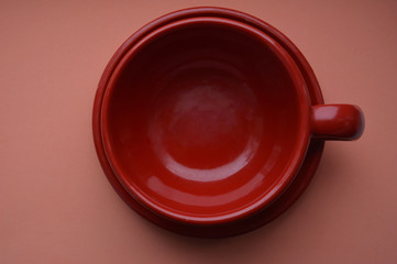 red ceramic cup (mug) and saucer on a coral background close-up isolated, top view