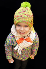 A little boy dressed in a warm hat and a warm sweater on a black background