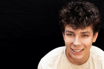 A guy with braces on his teeth in a white T-shirt on a black background and bristling hair on the head