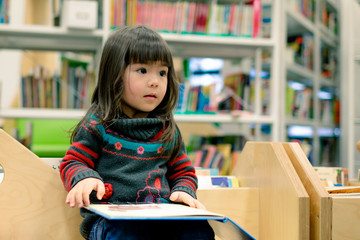 little girl reading a book in a library
