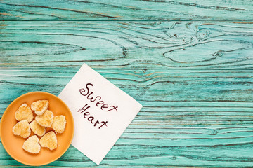 Saucer with heart-shaped cookies on a wooden turquoise background. A note with a wish is nearby. The concept of valenin day.