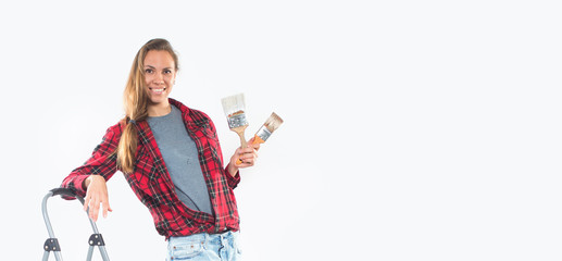 Smiling young woman with paintbrushes near empty wall