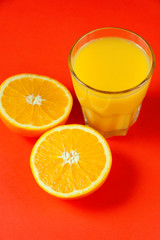 A glass of orange juice and a sliced ​​orange on a bright red background