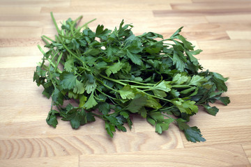 A large bundle of fresh parsley lies on the wooden surface of the table in the kitchen closeup view