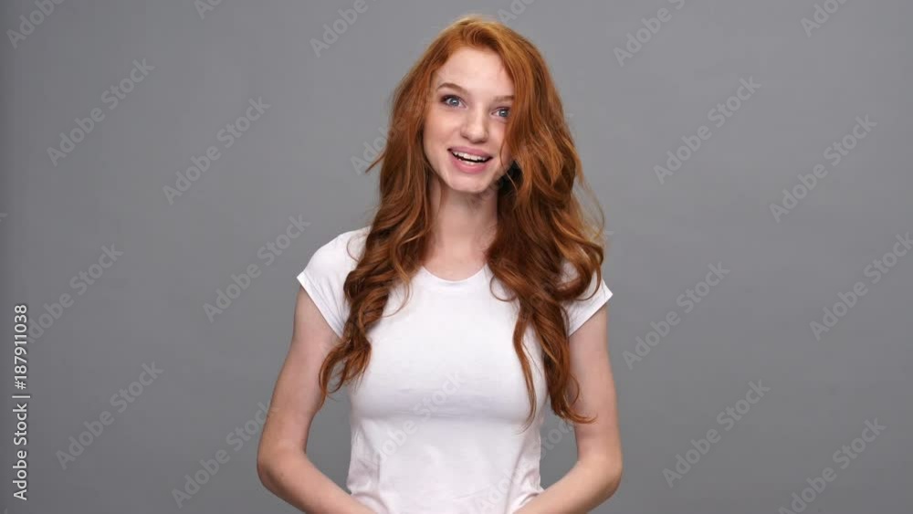 Sticker Surprised ginger woman in t-shirt looking at the camera and rejoice over gray background