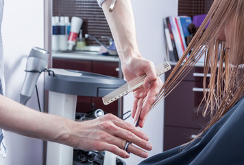 A hairdresser making haircut for a blonde female client in hairdressing salon