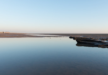 Beautiful sunny winters day on a british beach, with sand ripples and the sky reflecting in a water pool.