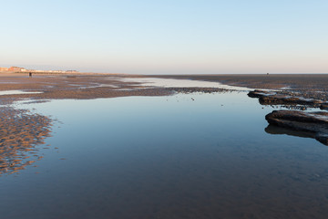 Beautiful sunny winters day on a british beach, with sand ripples and the sky reflecting in a water pool.