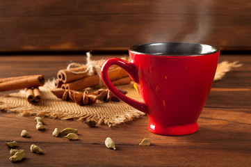 Red cup with coffee and steam, various spices on a wooden table