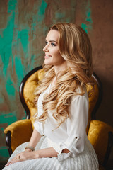 Fototapeta na wymiar Beautiful fashionable blond model girl with blue eyes is sitting in the vintage armchair, indoors