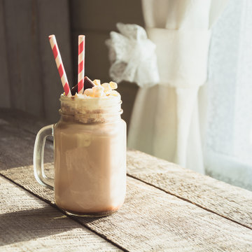 Chocolate coffee milkshake with whipped cream served in glass mason jar on gray wooden background. Summer sweet drink. Square image.