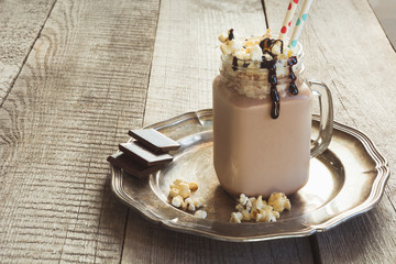 Chocolate coffee milkshake with whipped cream served in glass mason jar on gray wooden background. Summer sweet drink.