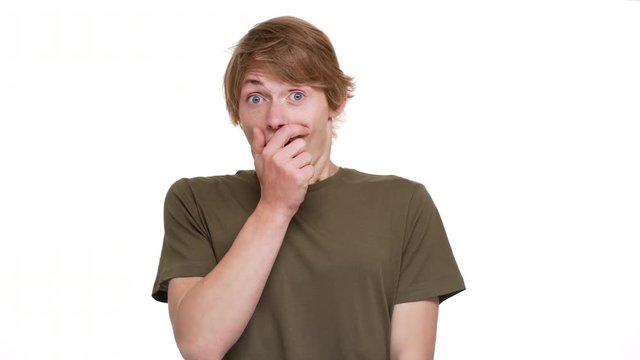 Portrait of surprised man being frightened covering open mouth with hand staring wide-eyed over white background closeup. Concept of emotions