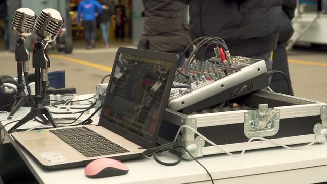 Laptop connected to a pair of microphones used by commentators, people in background.