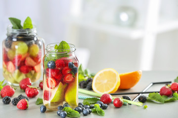 Mason jars of infused water with fruits and berries on table