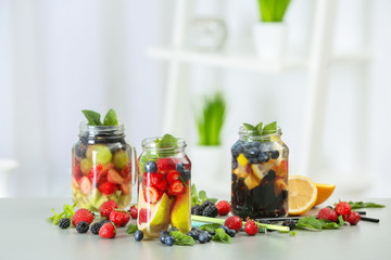 Mason jars of infused water with fruits and berries on table