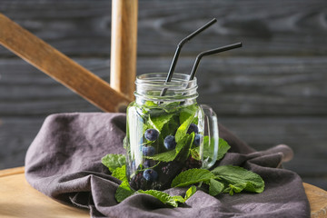 Jar of infused water with blueberry on chair against blurred wooden background