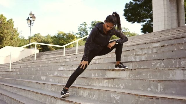 Beauty concentrated brunnete woman warming up on stairs before a training outdoors