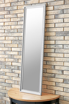 Modern mirror on stand near brick wall