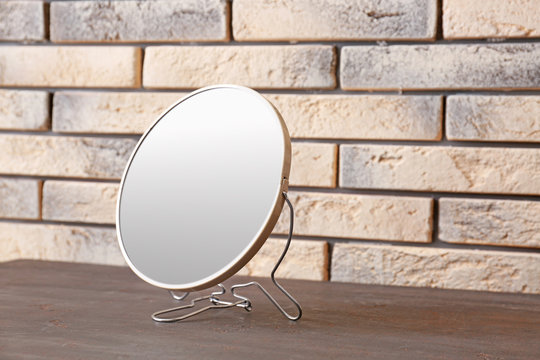 Modern mirror on wooden table near brick wall