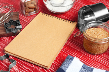 Kitchen utensils with ingredients for pastries and notebook on color wooden background