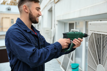 Male technician fixing air conditioner outdoors