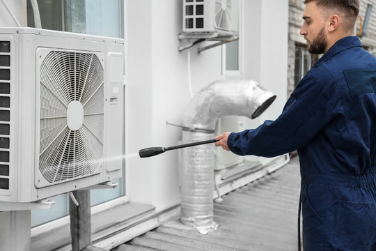Male technician cleaning air conditioner outdoors