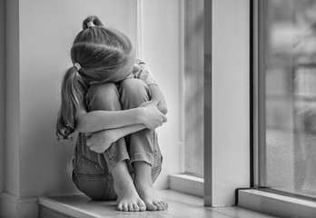 Sad little girl sitting on windowsill, black and white effect