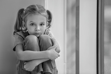 Sad little girl sitting on windowsill, black and white effect