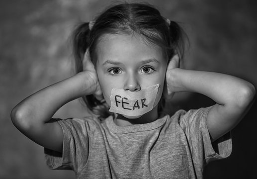 Sad little girl with taped mouth and word "Fear" on grey background, black and white effect