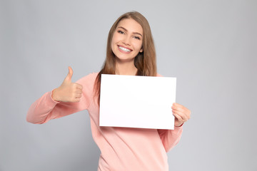 Fototapeta premium Young woman with blank sheet of paper on grey background