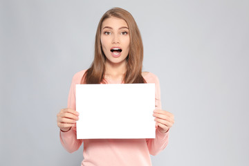 Fototapeta premium Emotional young woman with blank sheet of paper on grey background