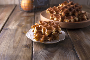 Sweet Belgian waffles for breakfast, on a wooden plate. On a brown wooden background