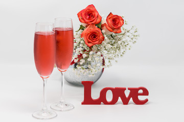 Two Glass of Rose Champagne, beautiful bouquet of blush roses and Love sign on white background.